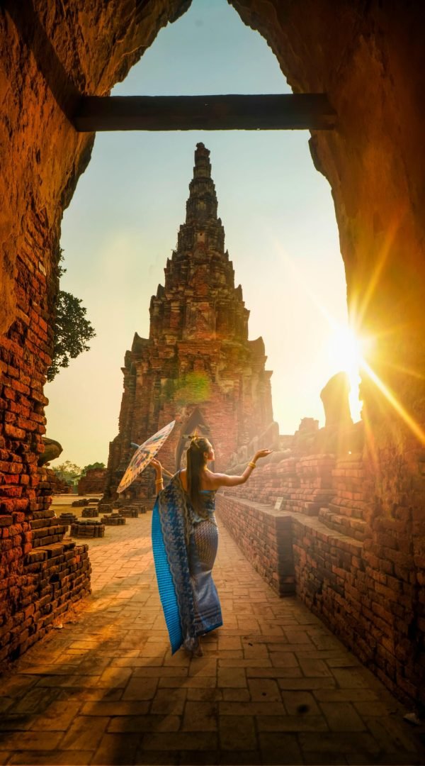 pexels-photo-2070485-2070485 A woman in traditional wear stands with an umbrella at a historic Ayutthaya temple during sunset.
